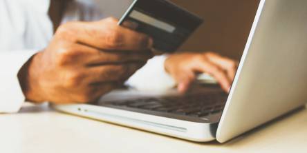 A man looking a credit card and putting the details into a laptop.